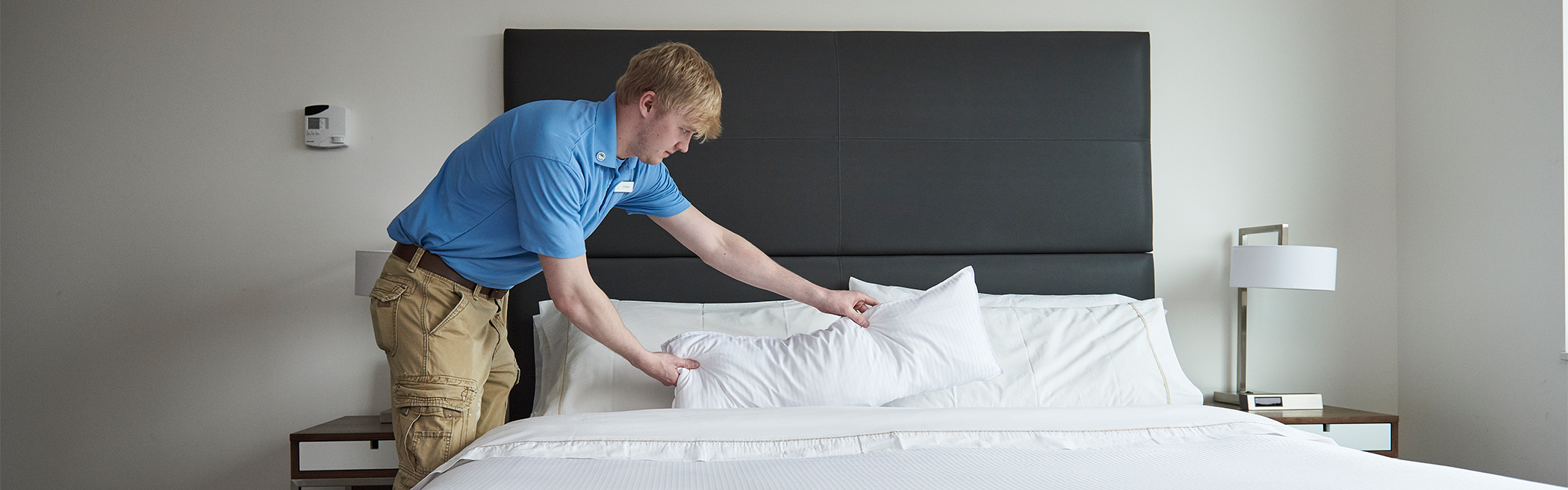A young man fixing a bed in a hotel room