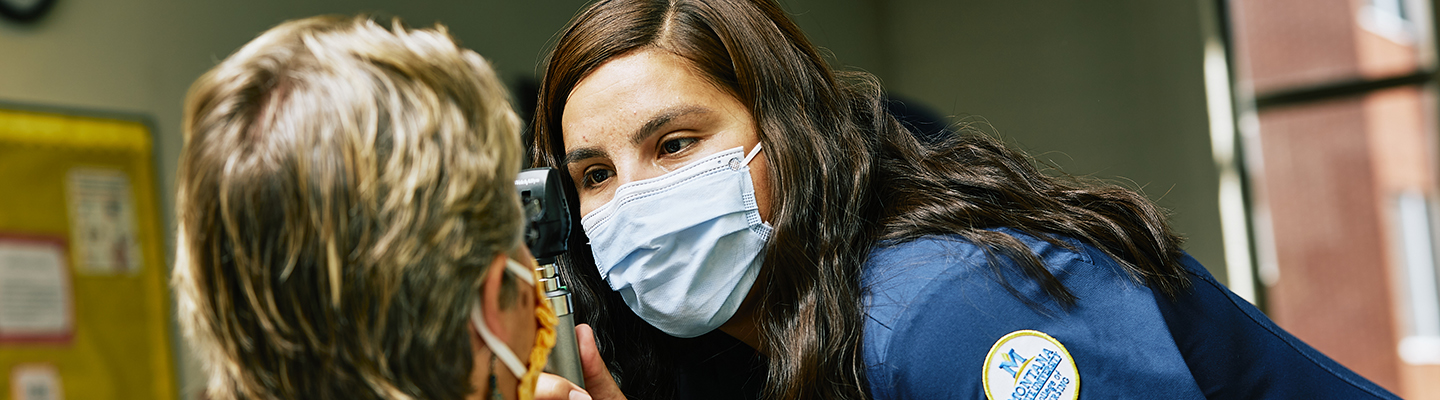 A young woman in PPE inspects a client's eyesight with equipment.