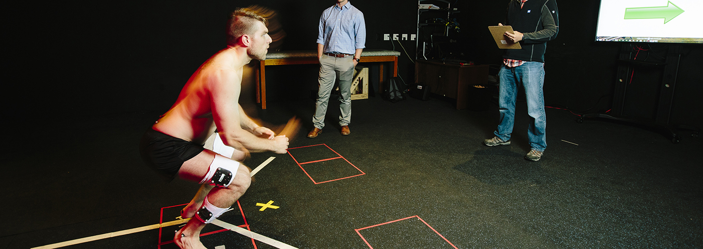 A young man with a series of sensors on him stands in front of researchers, ready to jump.