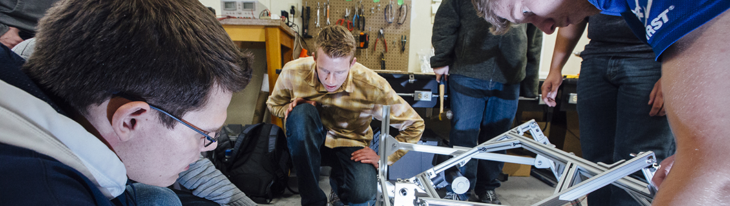 A group of students are bent over a rover intended for Mars, troubleshooting some construction issues.