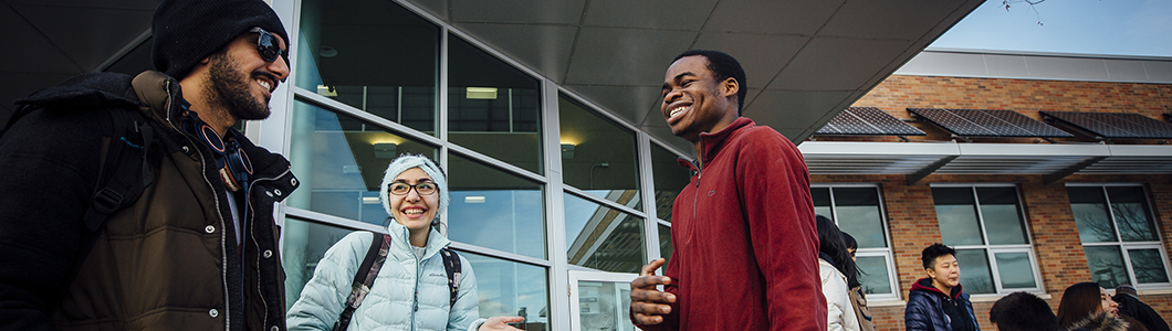 A group of students in winter clothing chat outside of the Strand Union Building on MSU Bozeman's campus.