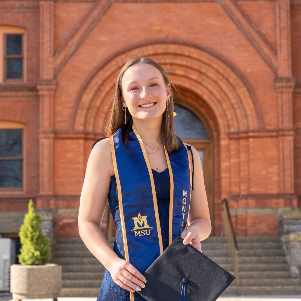 Emily Hagengruber with Graduation Regalia in front of Montana Hall