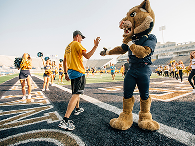 Students hi-fiving Champ as they walk onto the football field.