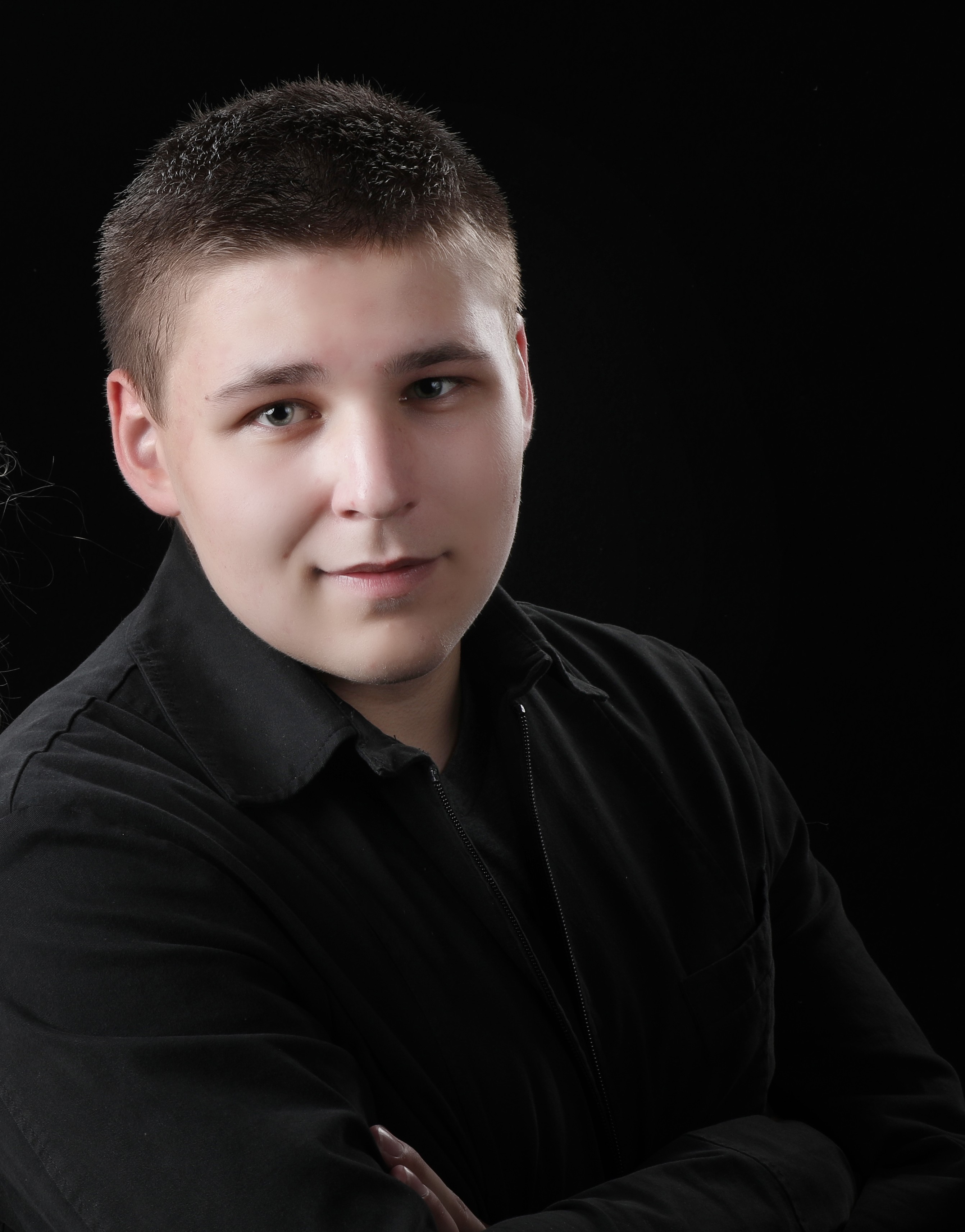 Young male with short brown hair wearing a black shirt with a black background