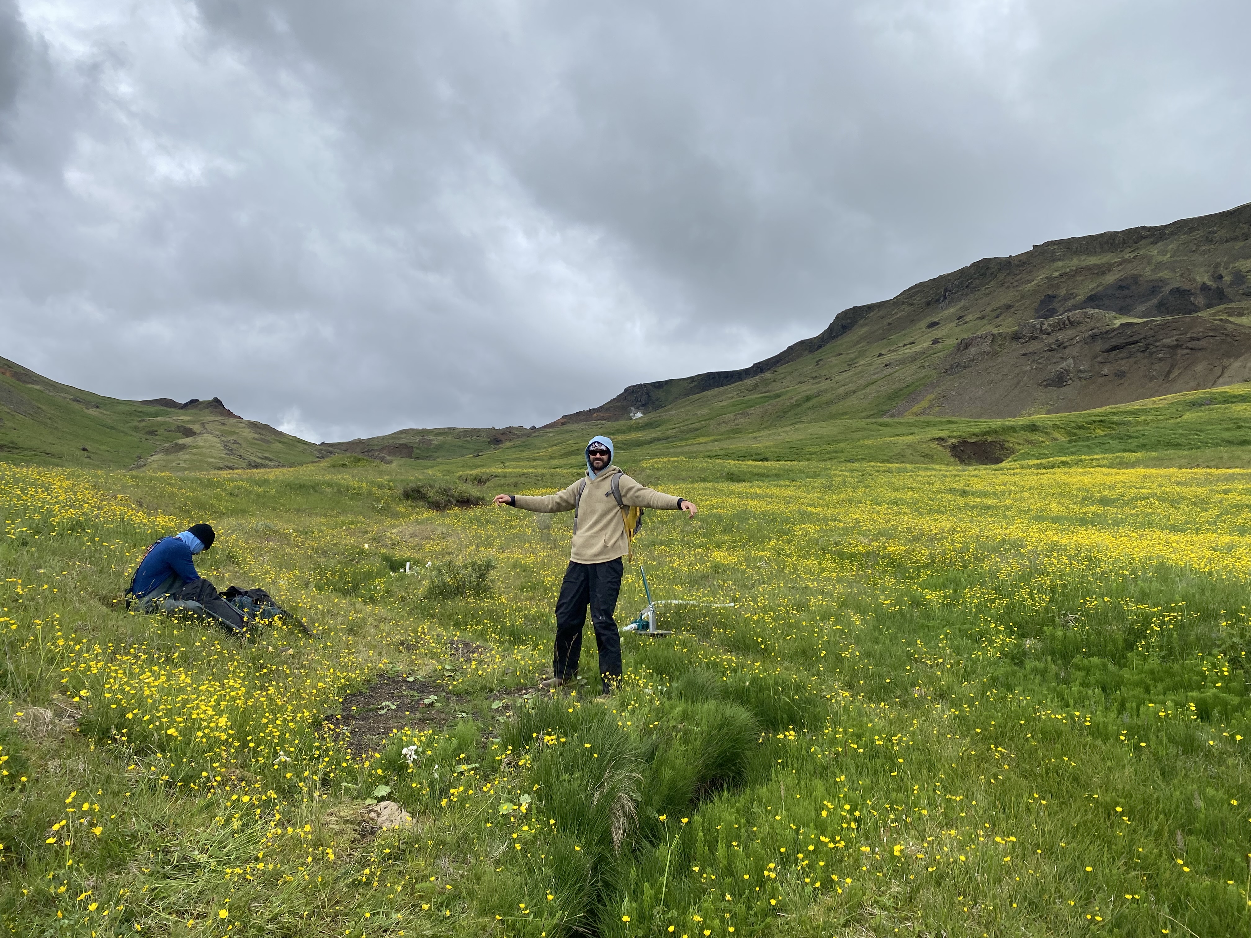 Researchers near a streambed standing in green grass and wildflowers under cloudy sky