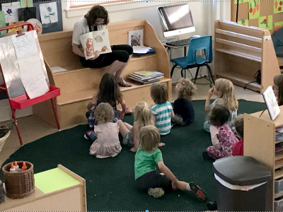 A group of young students listening to a teacher read a book