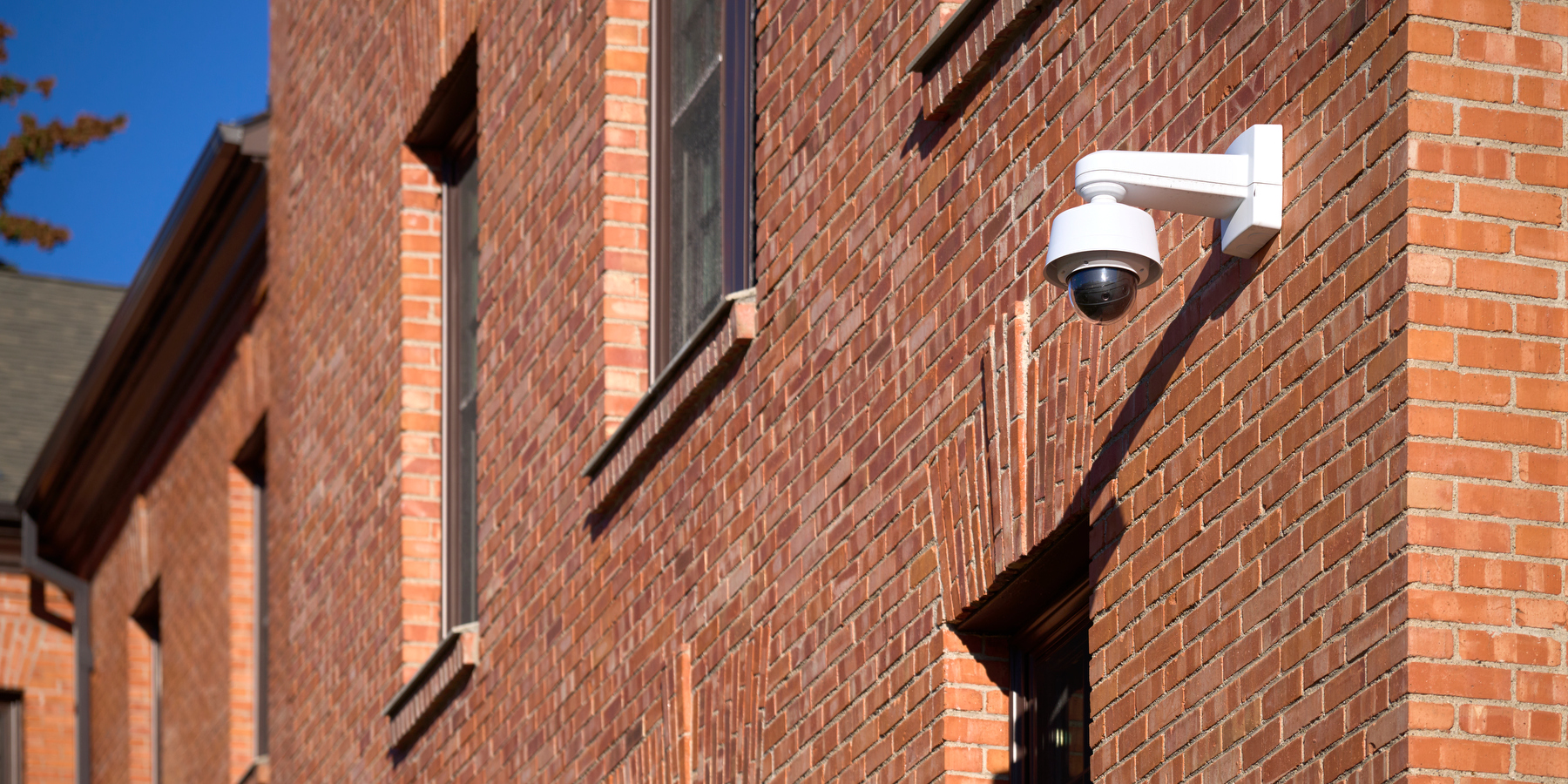 A white CCTV camera attached to the side of a brick building
