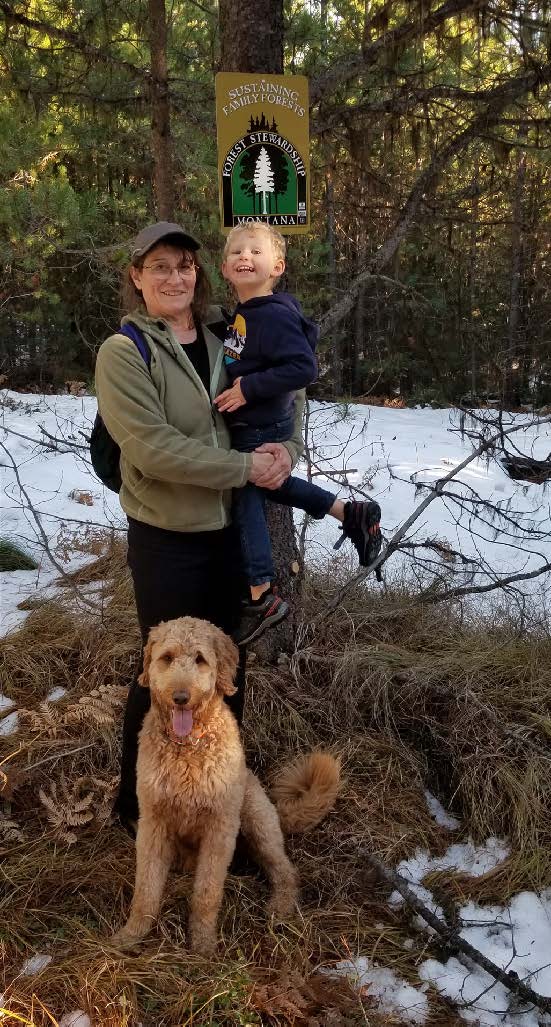 Image of Cindy Peterson holding a child with a golden colored dog sitting at her feet.