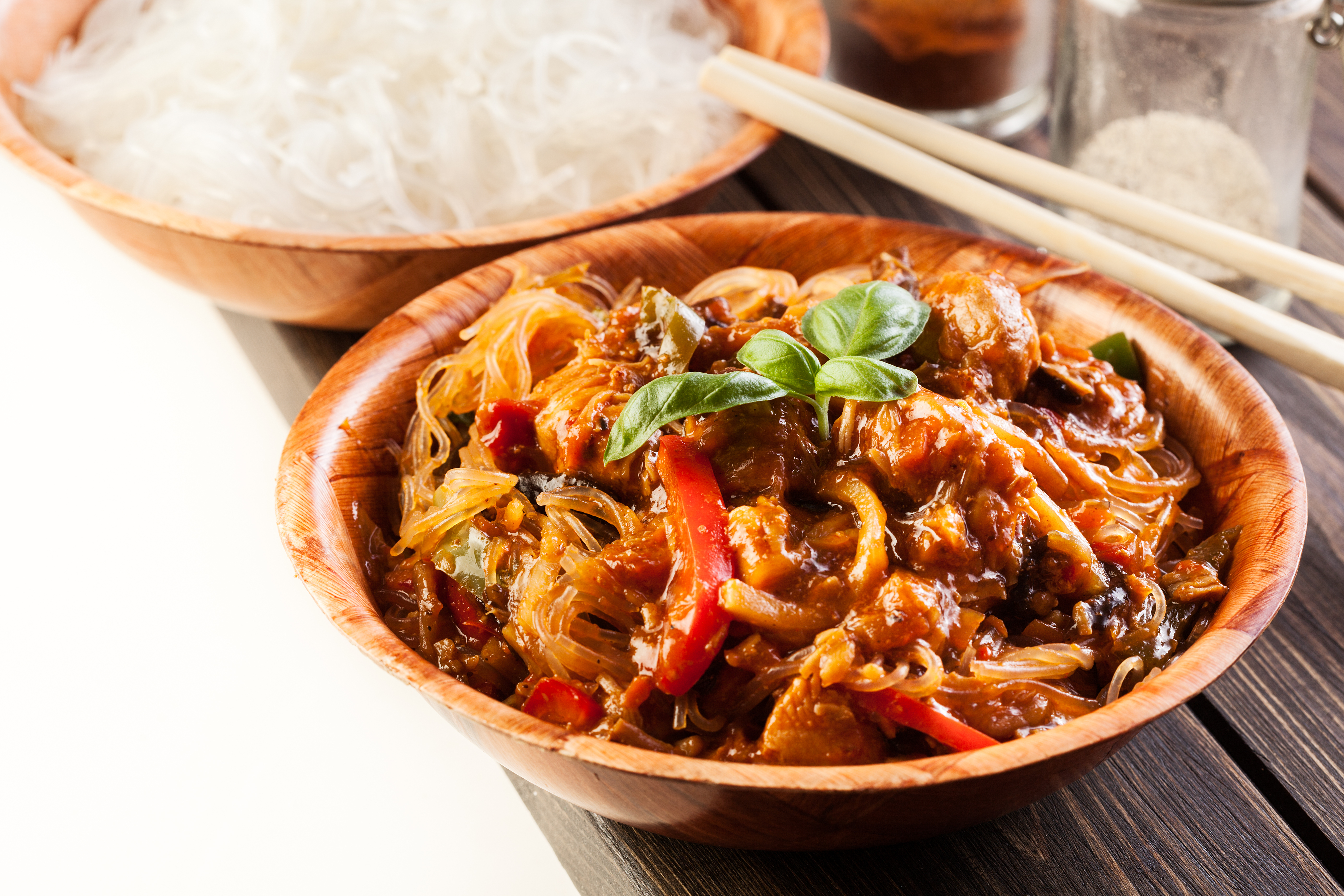 A wooden bowl with a chinese meal of noodles, meat, and vegetables.