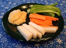 An image on lentil hummus on a black plate with carrot sticks, bell pepper slices, and cut jicama.