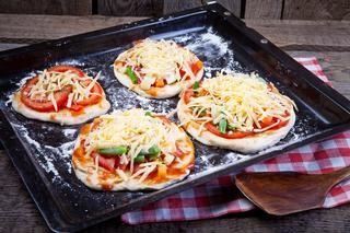 An image of four mini pizzas on a black baking sheet.