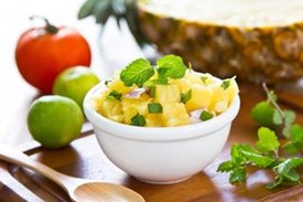 An image of summer fruit salsa in a white bowl on a table next to various fruits.