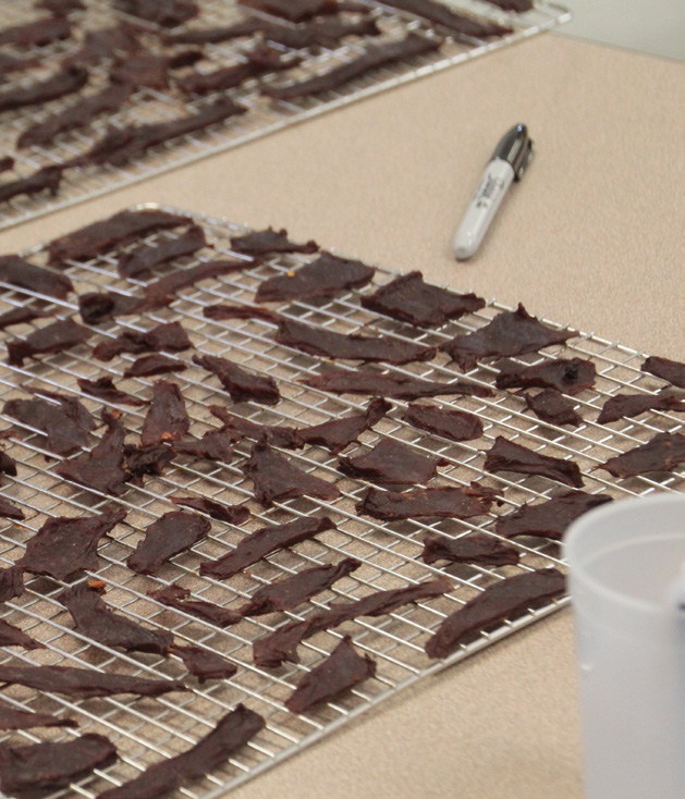 Freshly smoked jerky strips lie on the metal racks it was cooked on.