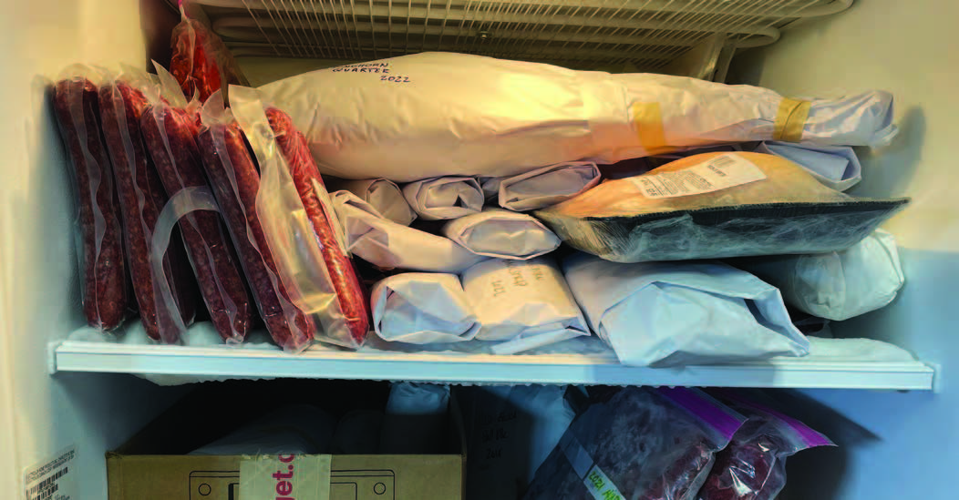 A freezer is open to display properly packaged meat in vacuum sealed plastic and butcher paper.