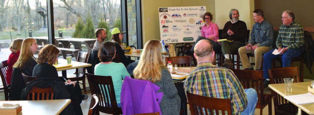 A group of people sit in chairs facing a panel of people speaking on rural vitality.