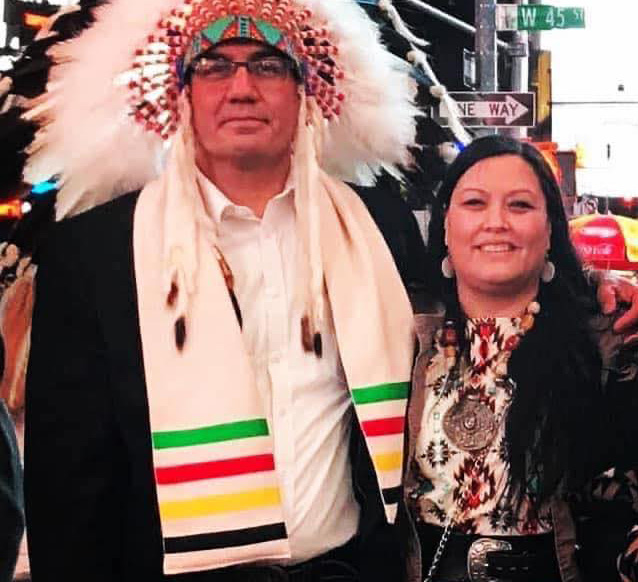 Tyson on the left with a Native American head piece on. Lona on the right is smiling and stands close to Tyson.