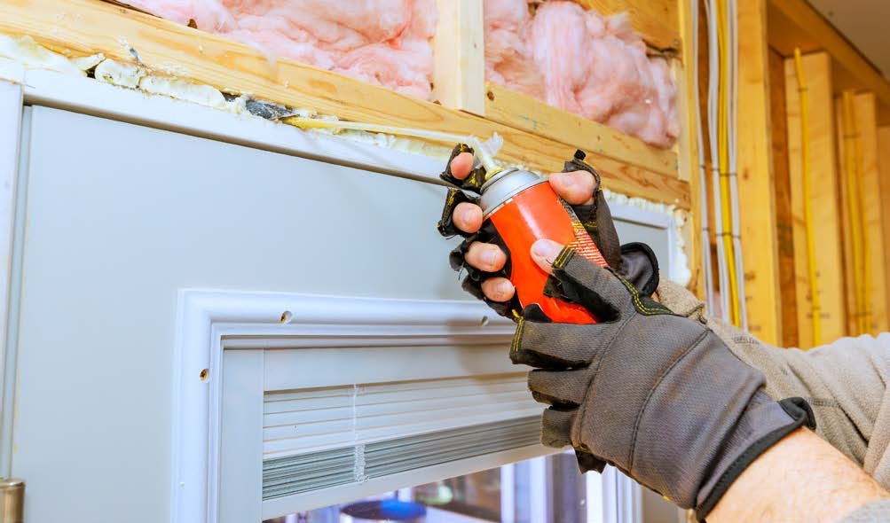 Two hands with gloves on hold a can of spray foam insulation above an exterior door