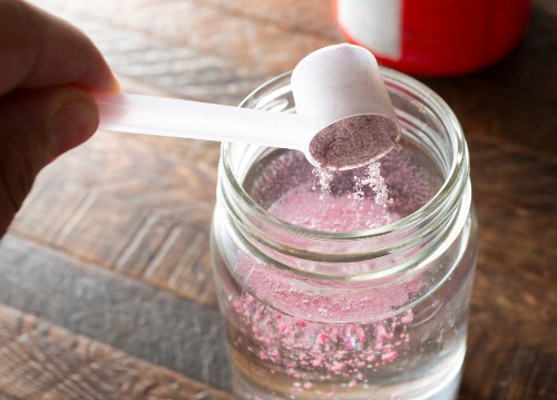 Powdered drink mix is being added to a glass of water with a plastic scoop
