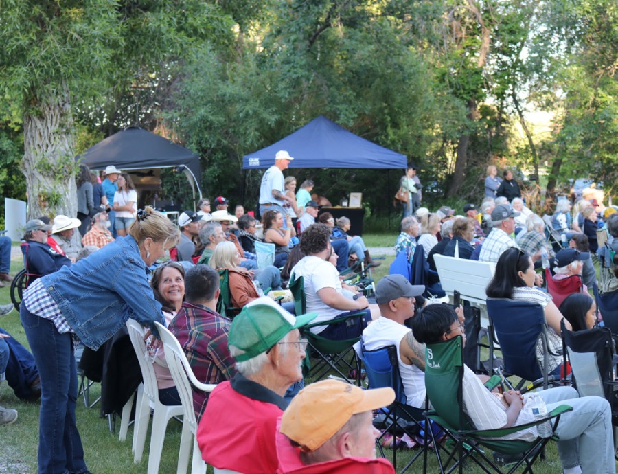Several people sit in rows to enjoy the outdoor concert and visit with one another