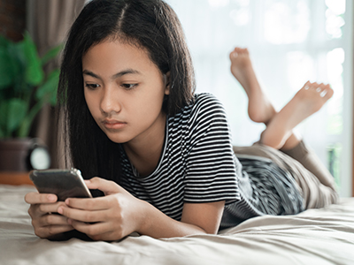 A young person is propped up on their elbows looking at a smartphone.