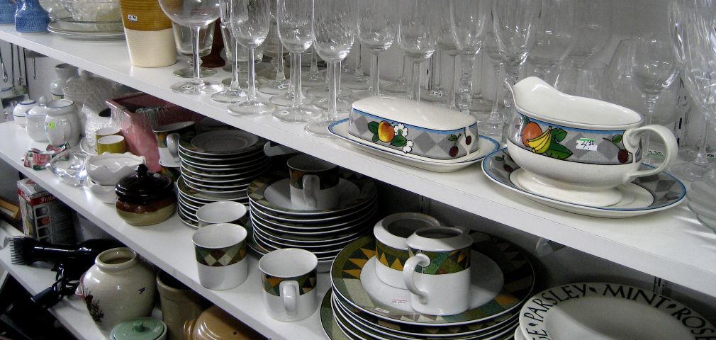 plates, glasses, mugs, and vases are stacked together on metal shelving