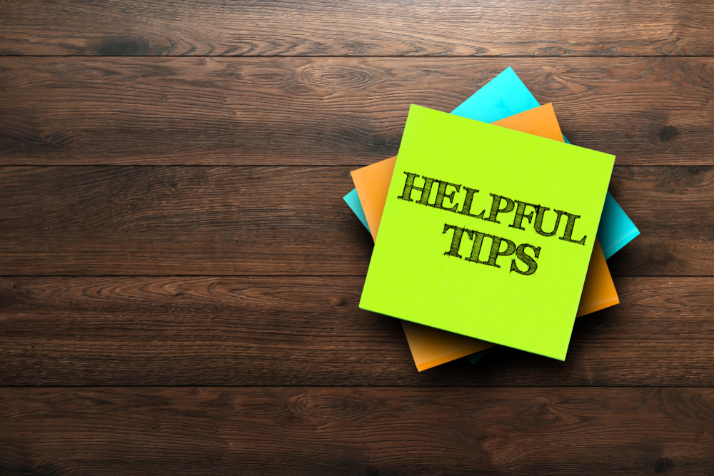 "Helpful Tips" written on top sticky note of a stack resting on a wooden desk.