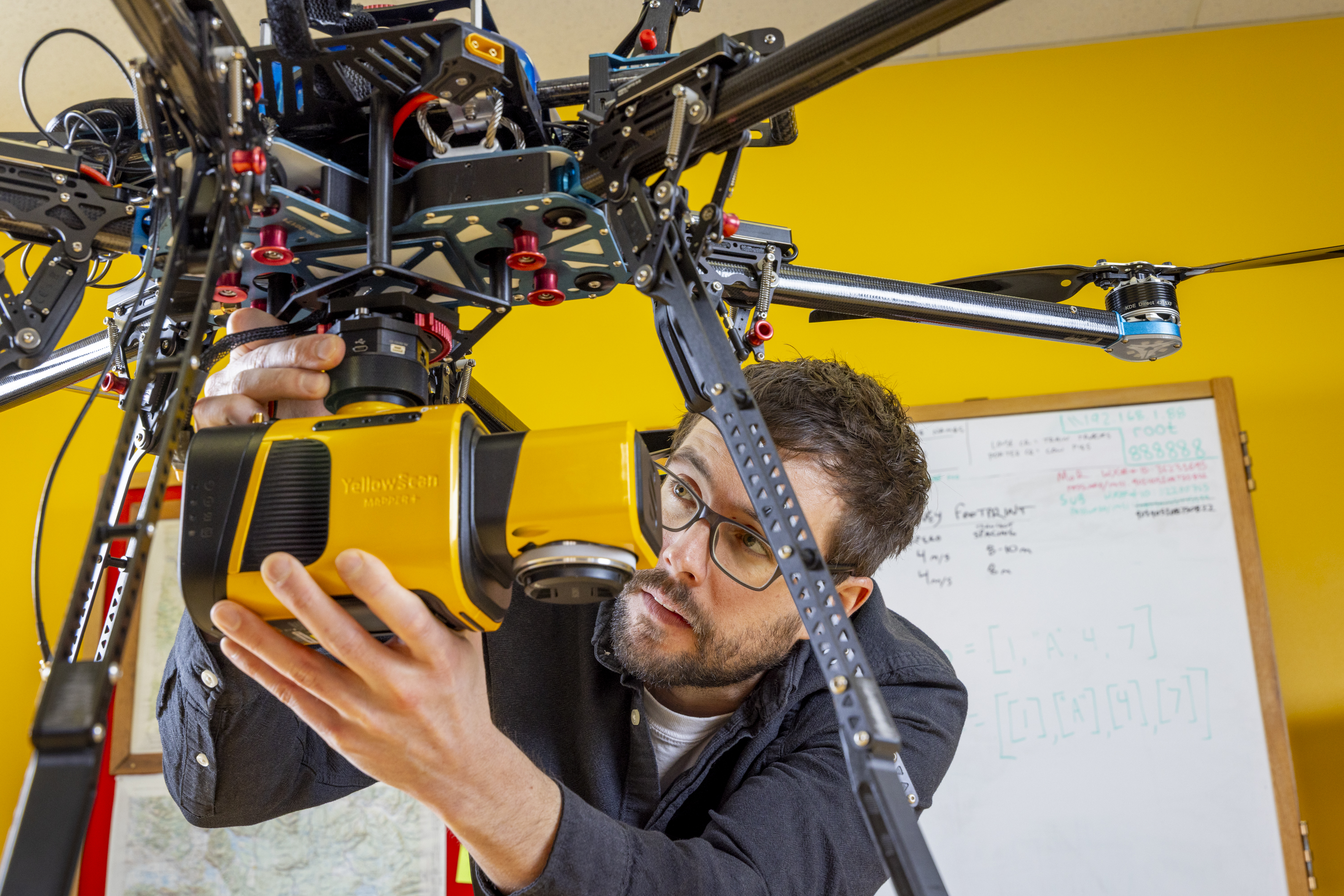 YellowScan Mapper + in the lab. A lab technichian is fixing it onto the drone
