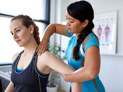 A female physical therapy assitant helps a patient stretch her shoulder.