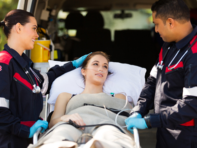 Two paramedics wheel a woman on a gurney into an ambulance. 