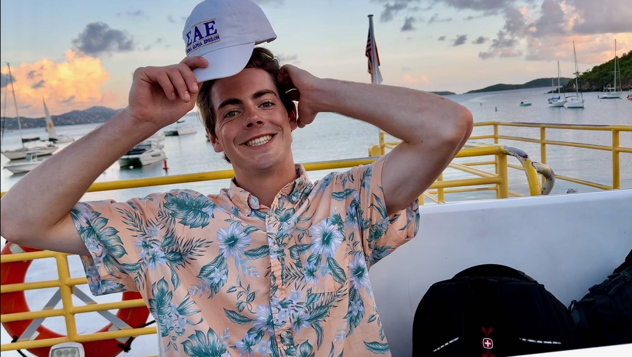 Male student sitting on a boat. There is a beautiful sunset behind him.
