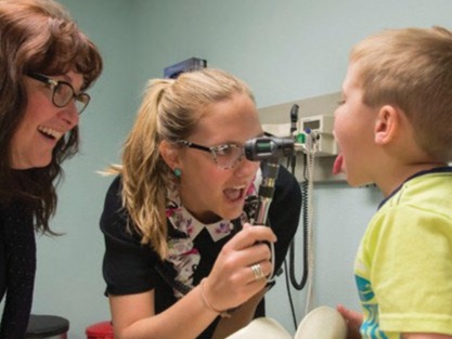 A medical student examines inside a young boy's mouth while a preceptor observes